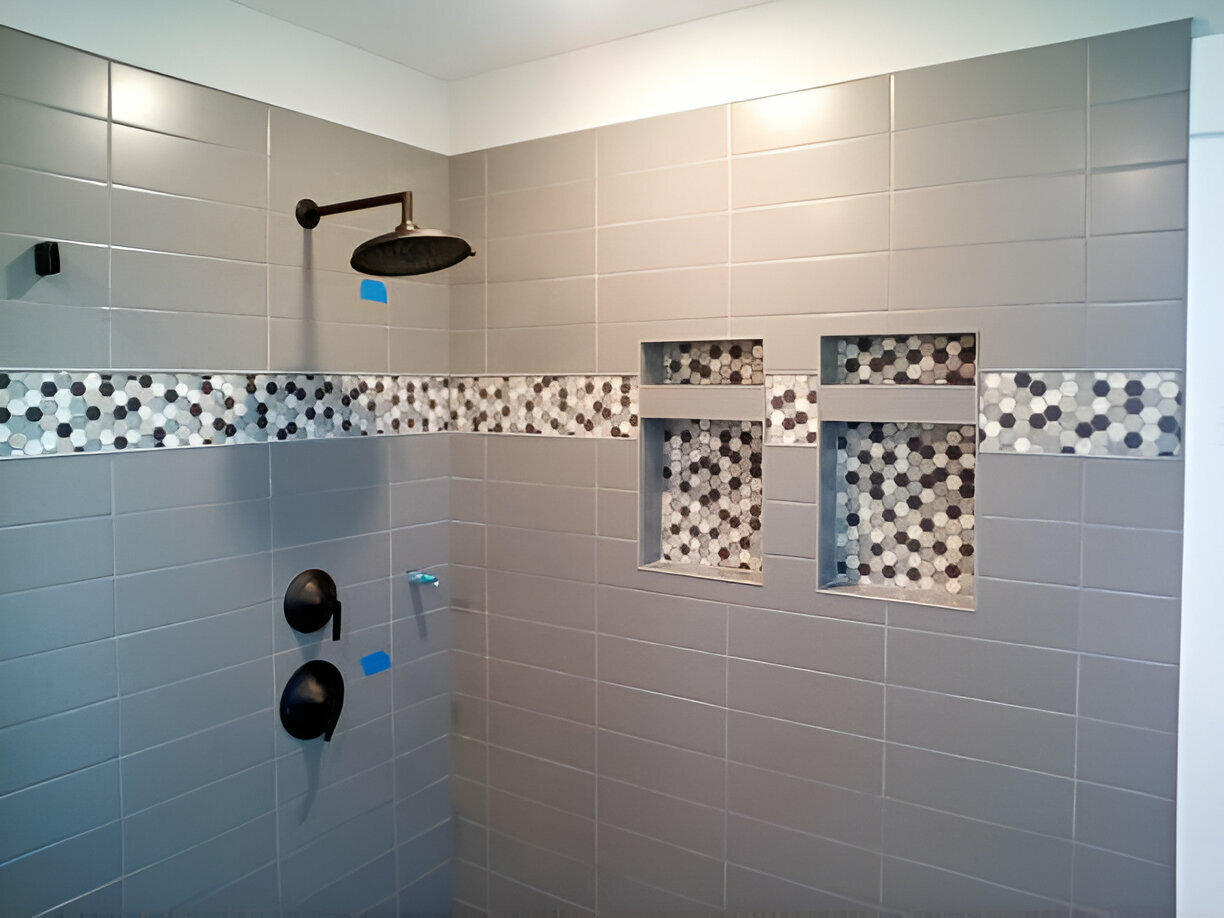 Gray tiled walk-in shower with black rain showerhead, built-in storage niches, and decorative hexagonal tile accents