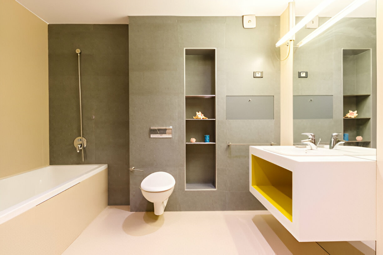 Minimalist modern bathroom with floating toilet, built-in shelves, bathtub, and a stylish vanity with yellow storage accent