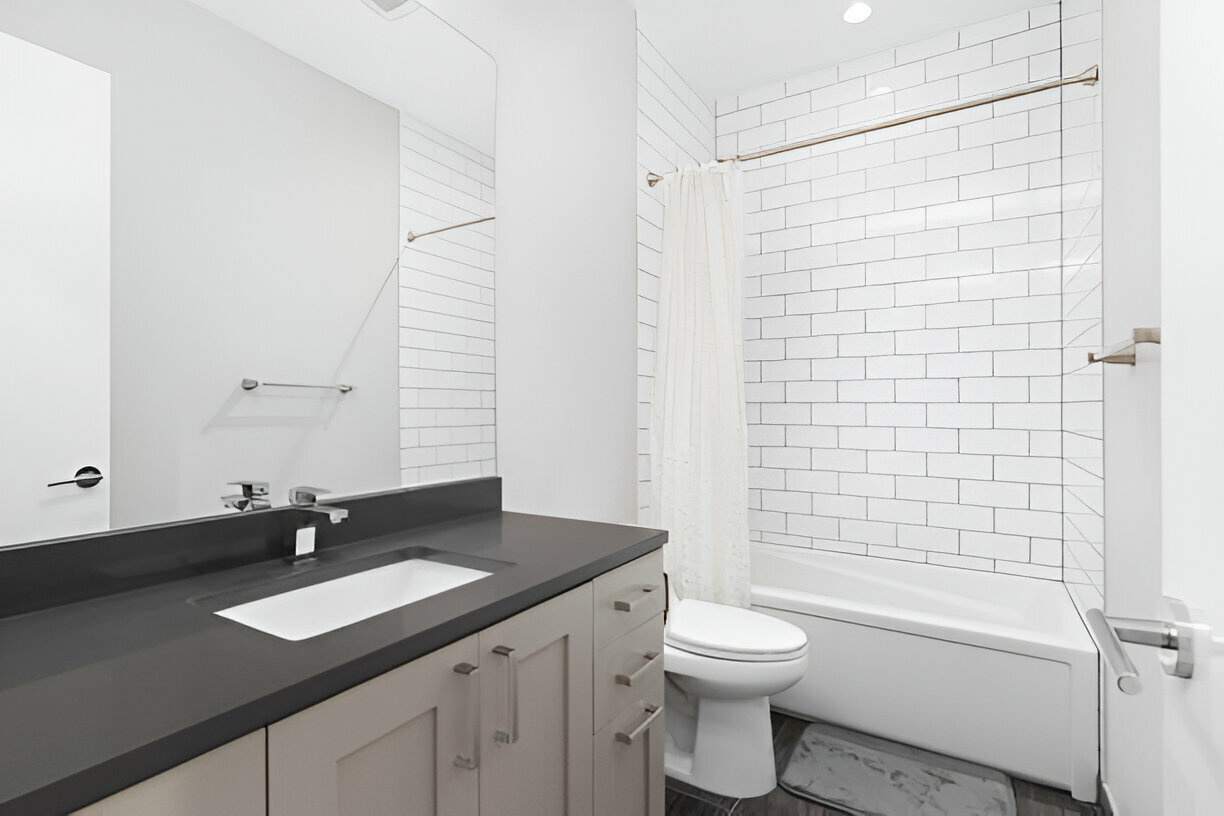 Modern bathroom featuring a dark gray vanity countertop, white subway tile bathtub-shower combination, and minimalist décor with neutral colors