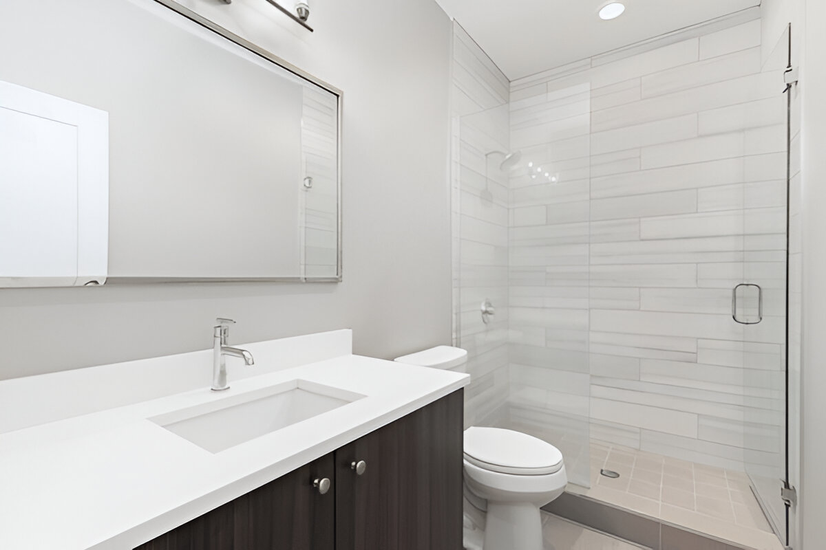 Contemporary bathroom featuring dark wood vanity with white countertop, modern fixtures, and a glass-enclosed walk-in shower with horizontal tiles