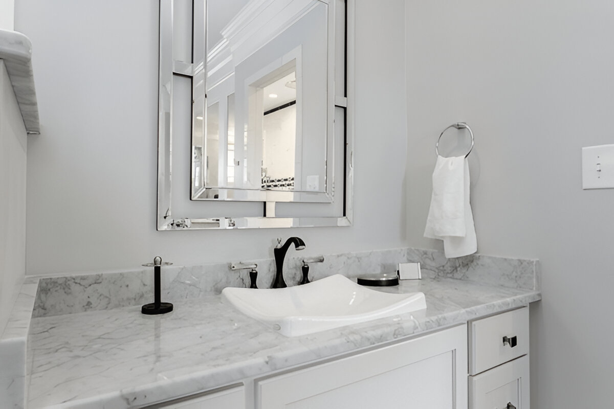 White bathroom vanity featuring marble countertop, uniquely shaped vessel sink, matte black faucet, and decorative rectangular mirror with chrome accents