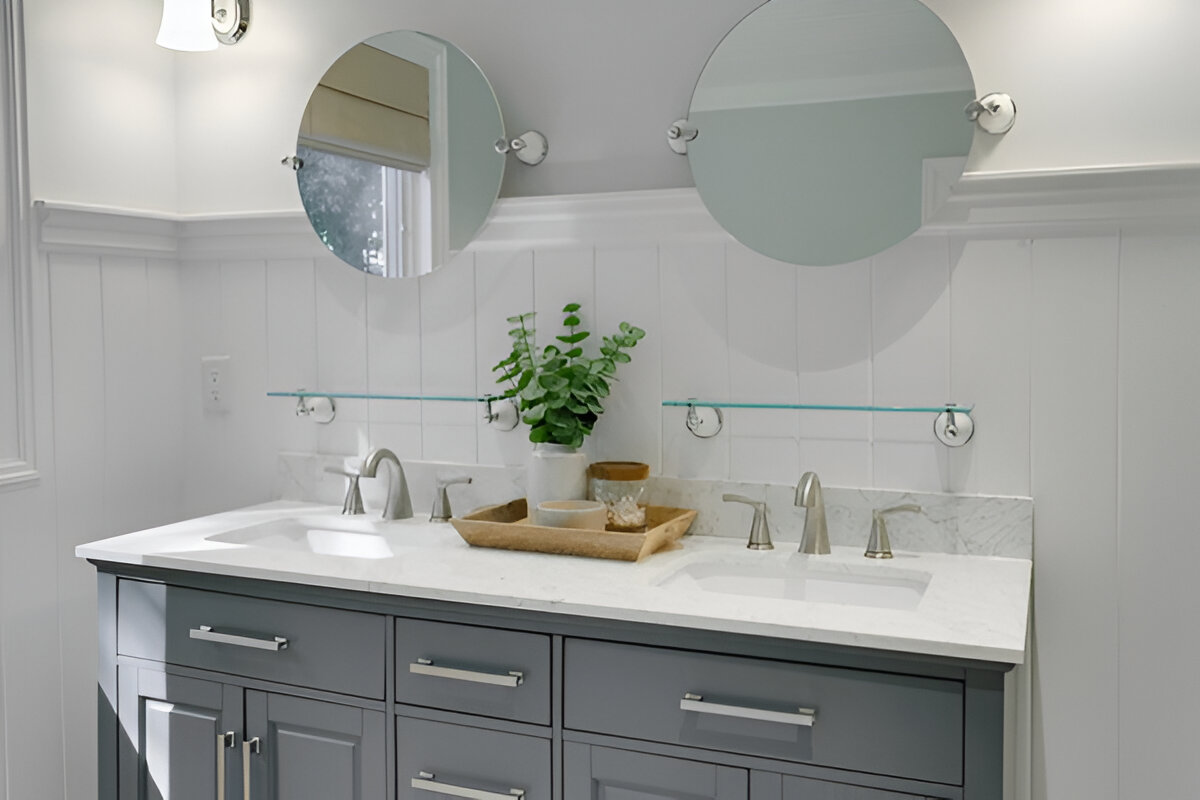 Gray double vanity with a white marble countertop, round mirrors, brushed nickel faucets, and wainscoting in a classic bathroom