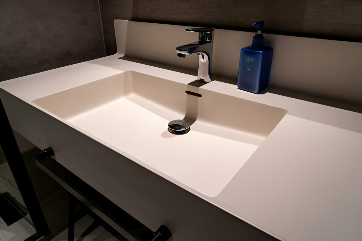 Minimalist bathroom sink with an integrated basin, chrome faucet, white countertop, and a blue soap dispenser in a modern setting