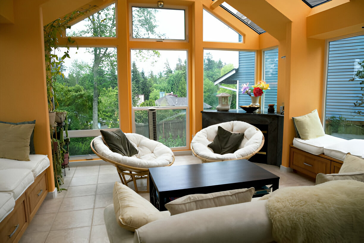 Bright sunroom with orange walls, cozy seating, and large windows