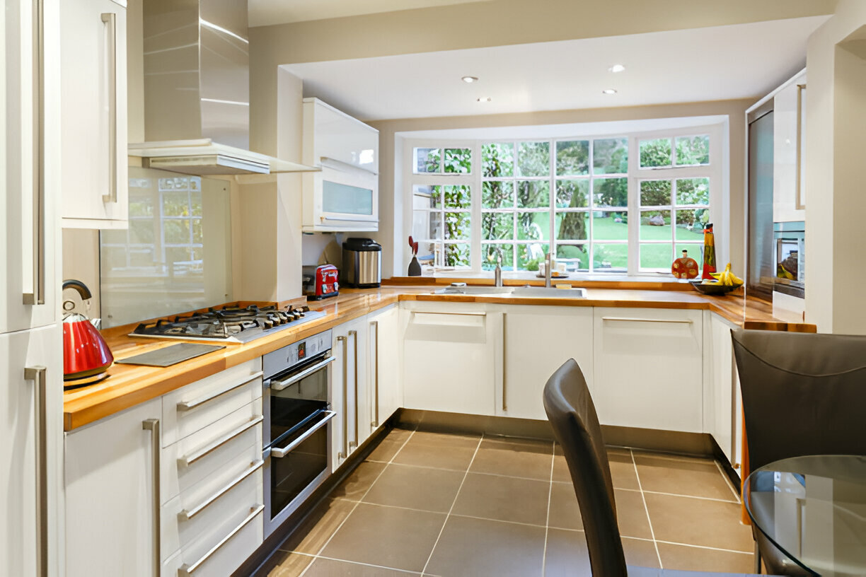 Modern kitchen with white cabinets, wooden countertops, and garden view