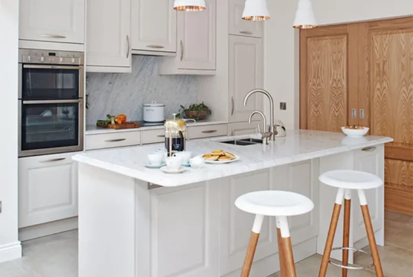 Airy white small kitchen featuring a kitchen island with marble countertop, wooden bar stools, and built-in cabinets.
