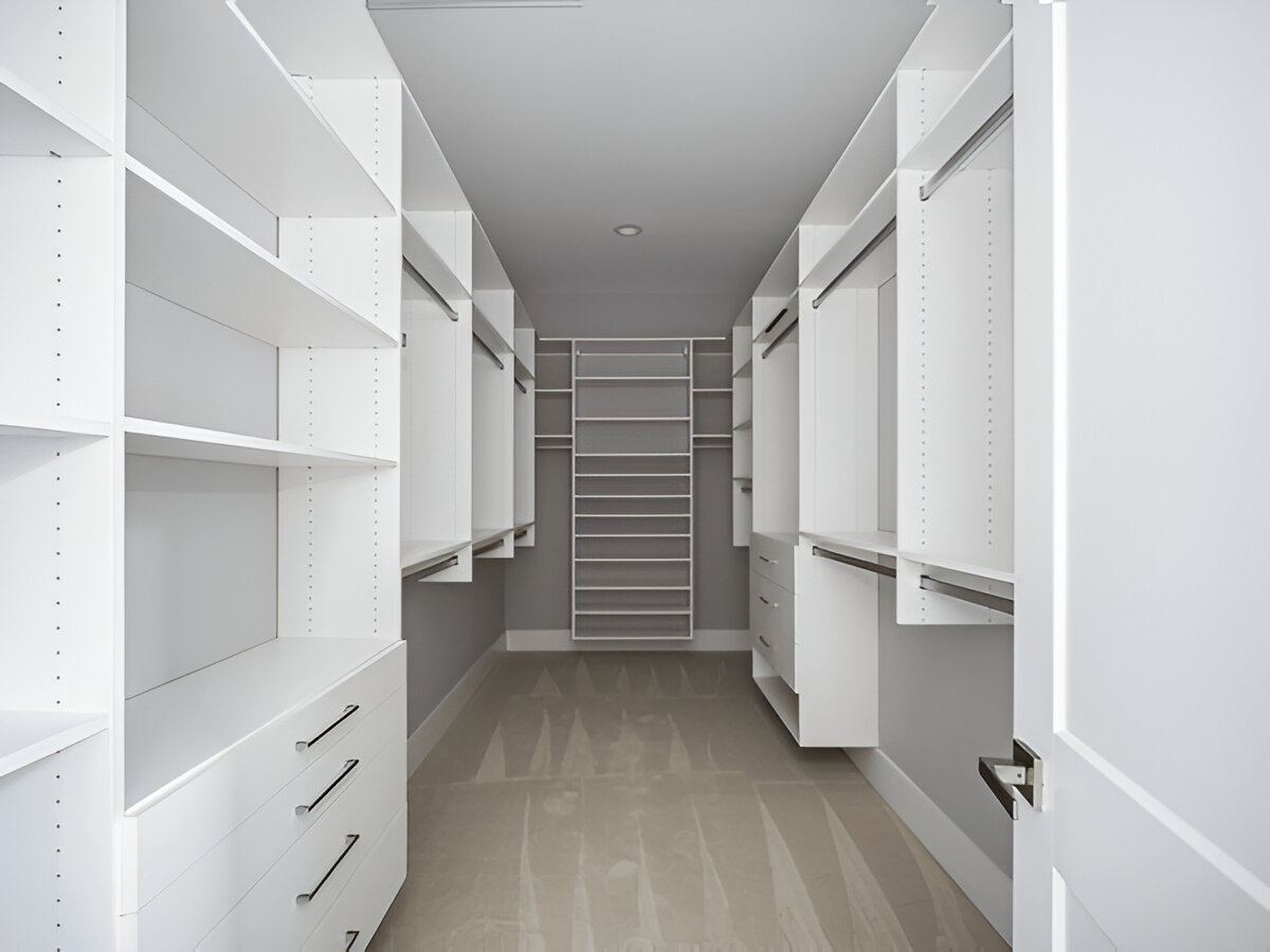 Empty white walk-in closet with shelves, drawers, and hanging rods on both sides.