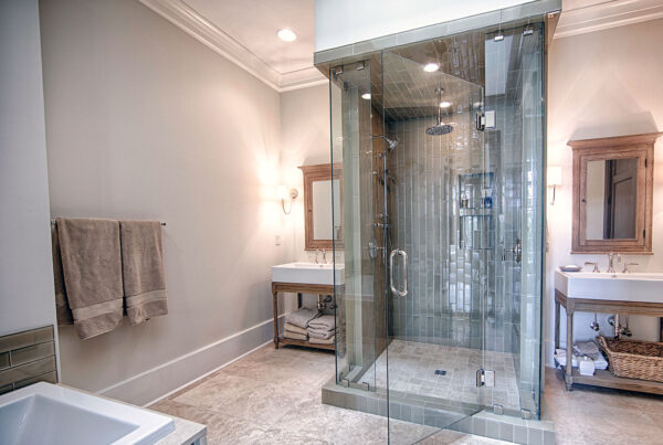 A spacious bathroom with a large glass-enclosed shower, double vanity sinks, and a freestanding bathtub. The room features neutral tones, wood accents, and recessed lighting
