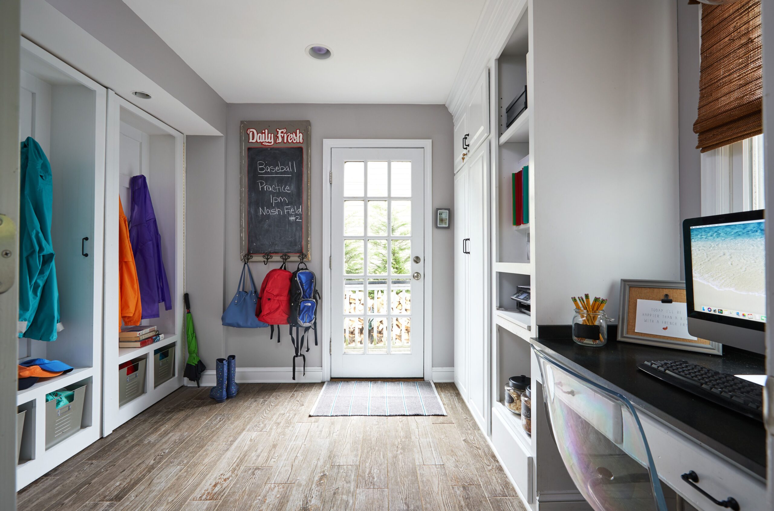 Mudroom featuring wall hooks, open cubbies with jackets and bins, a chalkboard with a message, and a built-in desk with a computer and shelves