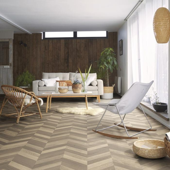 Cozy living room featuring chevron-patterned vinyl flooring, wood-paneled accent wall, neutral sofa, indoor plants, and woven textures