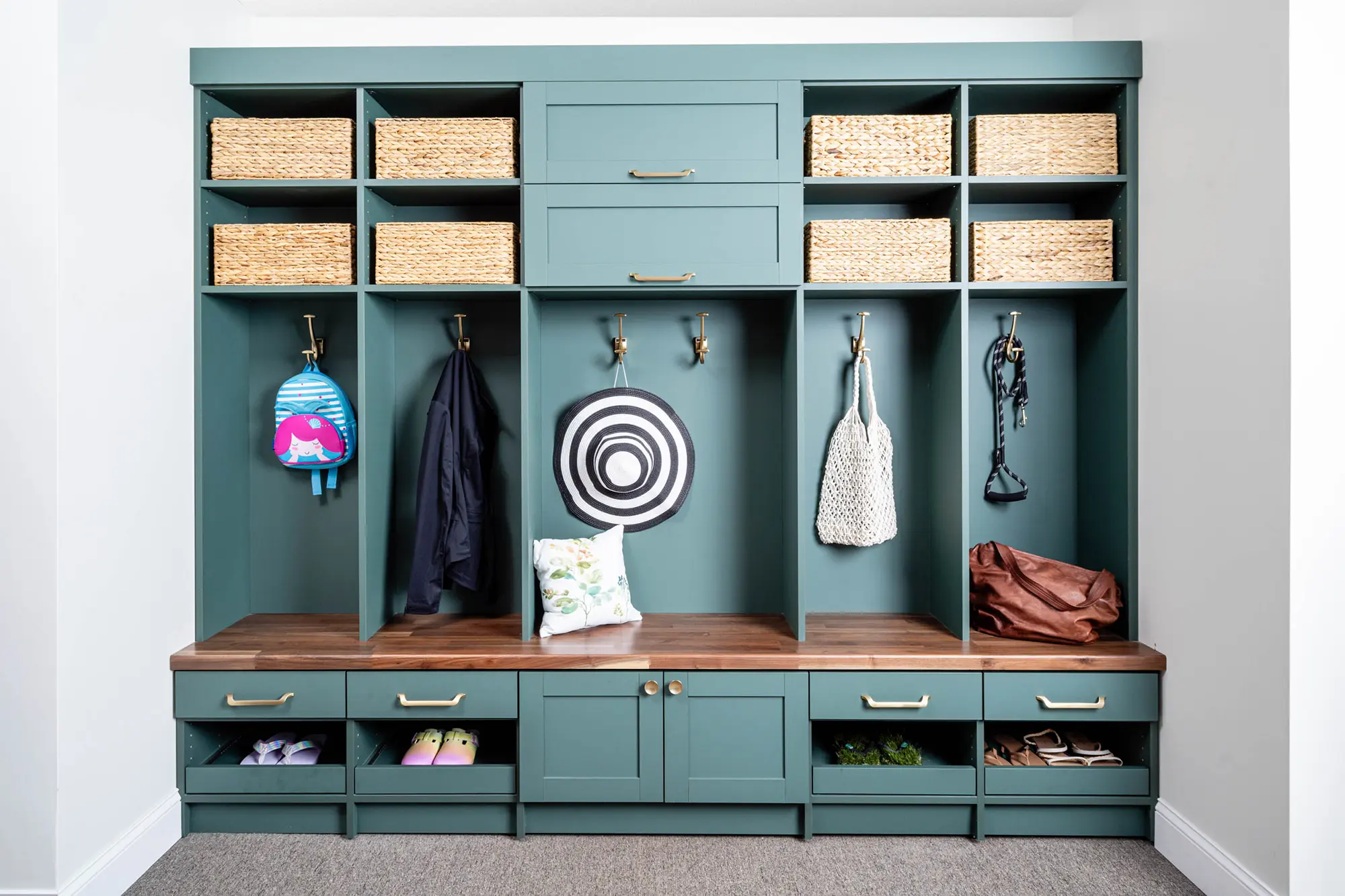 Built-in teal mudroom lockers with wooden bench, gold hooks, upper basket storage, and open cubbies for shoes