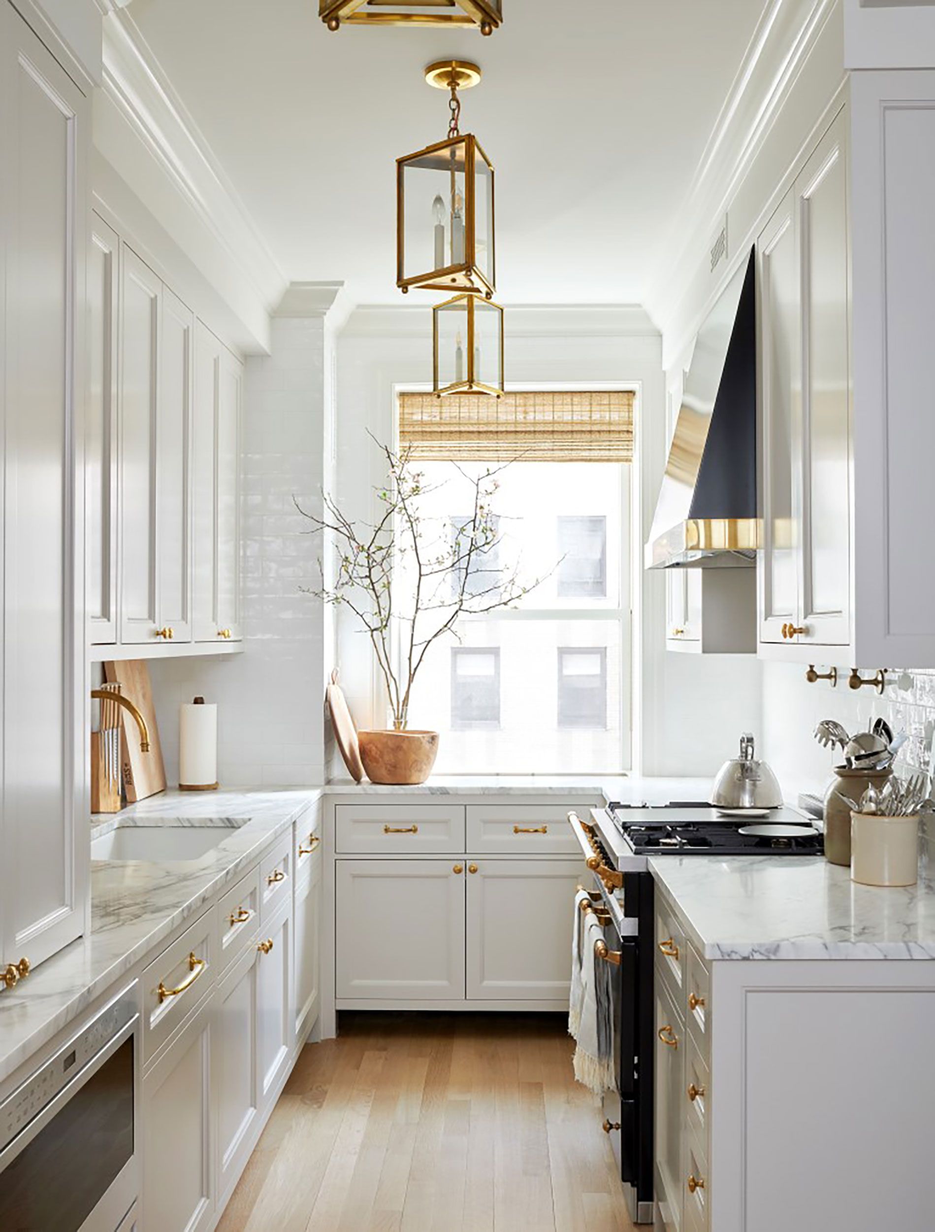 Chic galley kitchen featuring white cabinetry, marble countertops, gold hardware, and a large window with natural light.