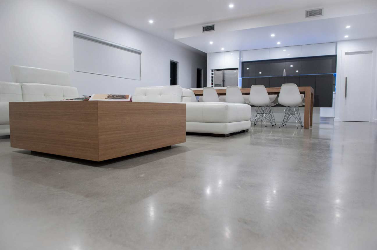 Modern living room with polished concrete floors, white leather sofas, wooden coffee table, and open kitchen with white dining chairs