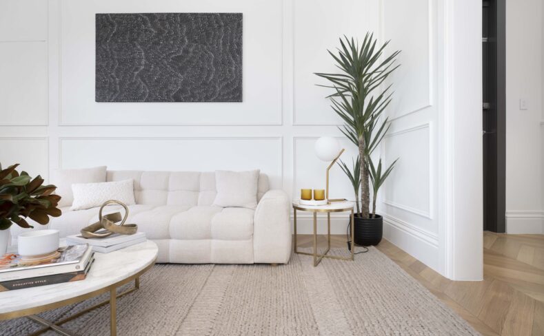 Bright minimalist living room featuring white wall paneling, a cream tufted sofa, indoor plant, round coffee table, and modern accessories
