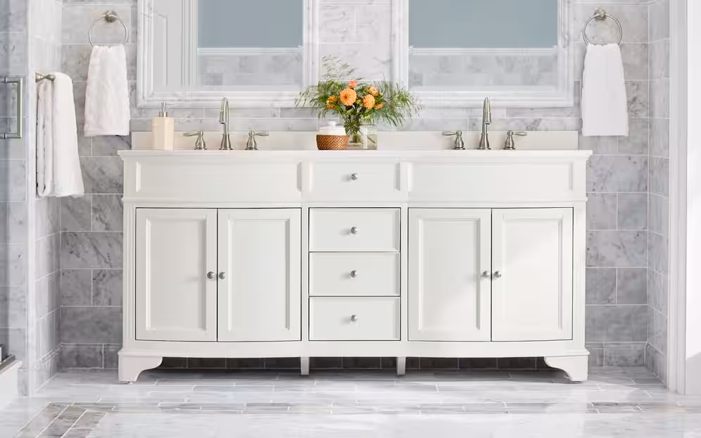 Stylish bathroom vanity with terrazzo backsplash, wood cabinetry, two white vessel sinks, gold faucets, and arched mirrors.