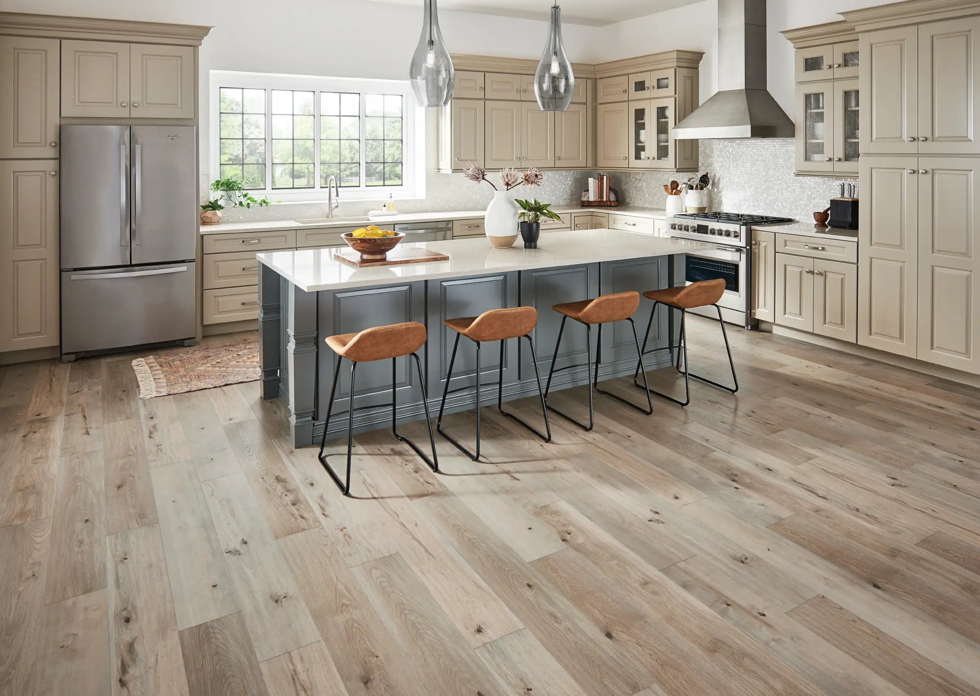 Spacious kitchen featuring light wood-look laminate flooring, beige perimeter cabinets, a gray island, and leather bar stools.