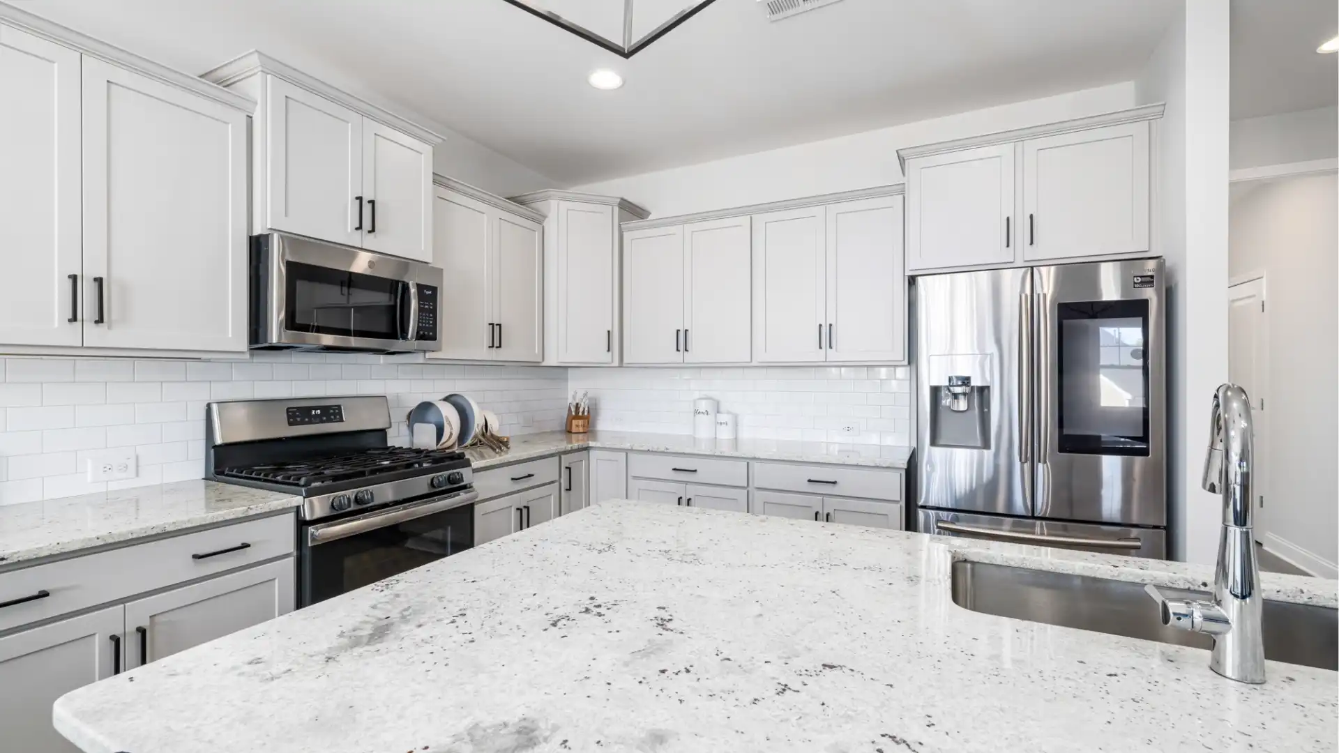 Contemporary kitchen featuring white quartz countertops, light gray shaker cabinets, stainless steel appliances, and subway tile backsplash.