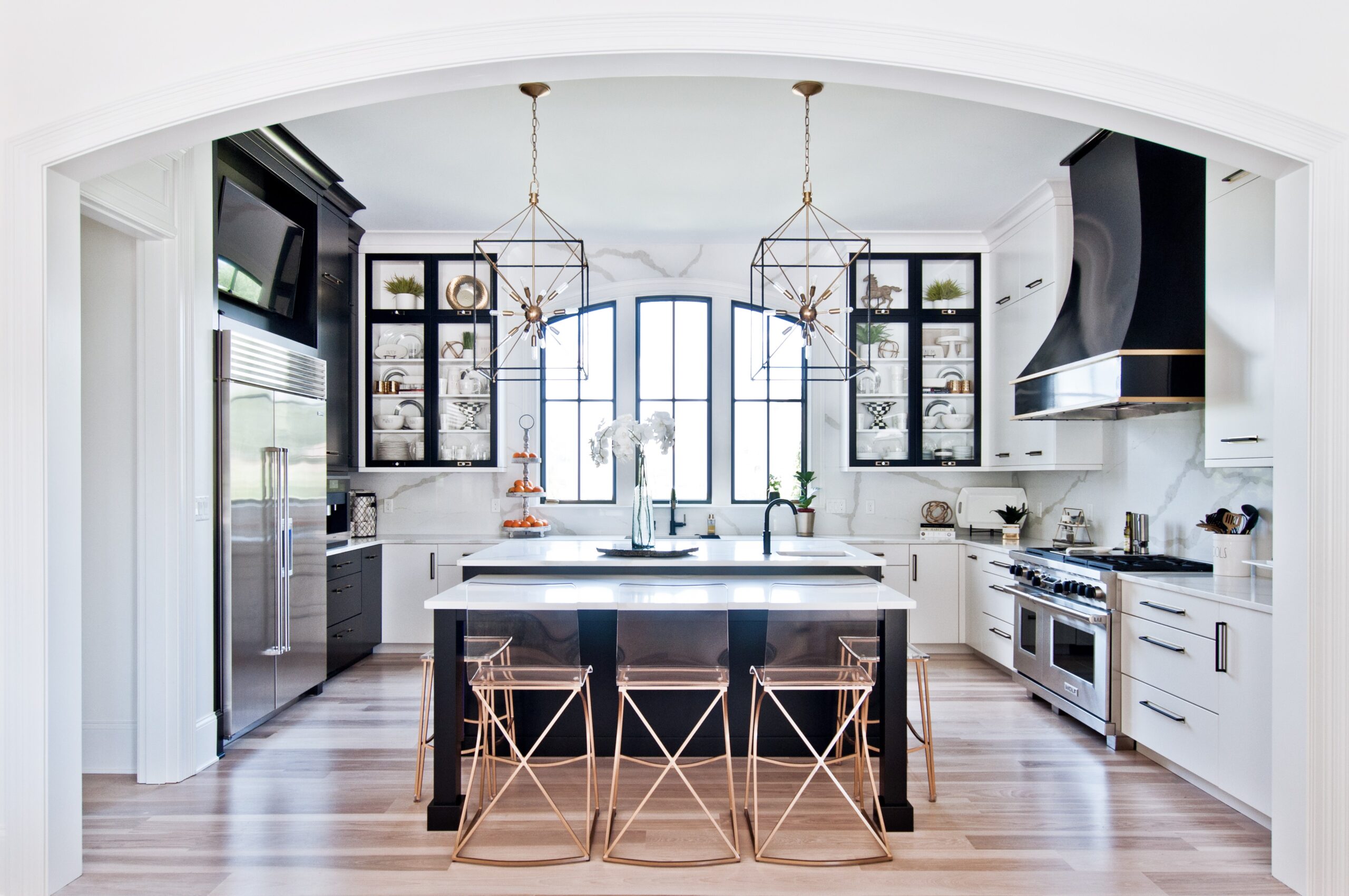 Modern black and white kitchen with central island, gold pendant lights, and transparent bar stools
