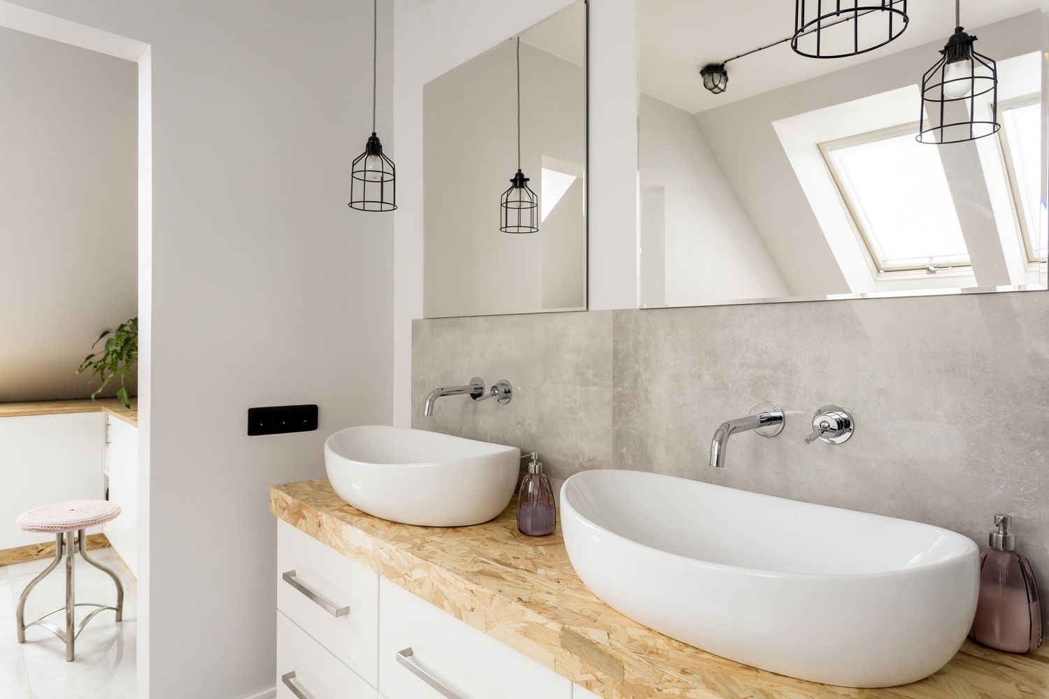 Minimalist bathroom featuring two white oval vessel sinks on a raw wood countertop, wall-mounted chrome faucets, and modern cage pendant lights.