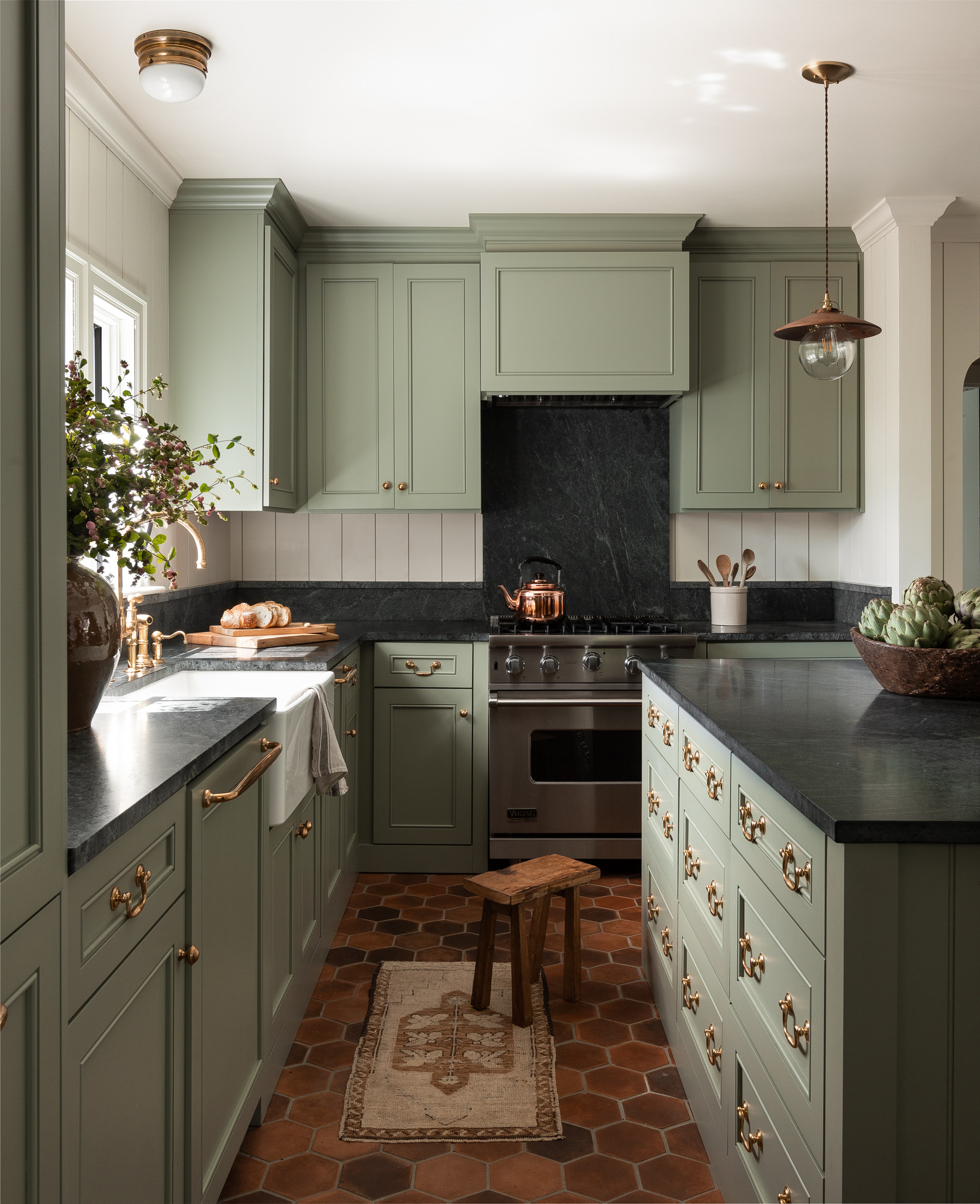 Classic kitchen with sage green cabinets, black countertops, and copper accents