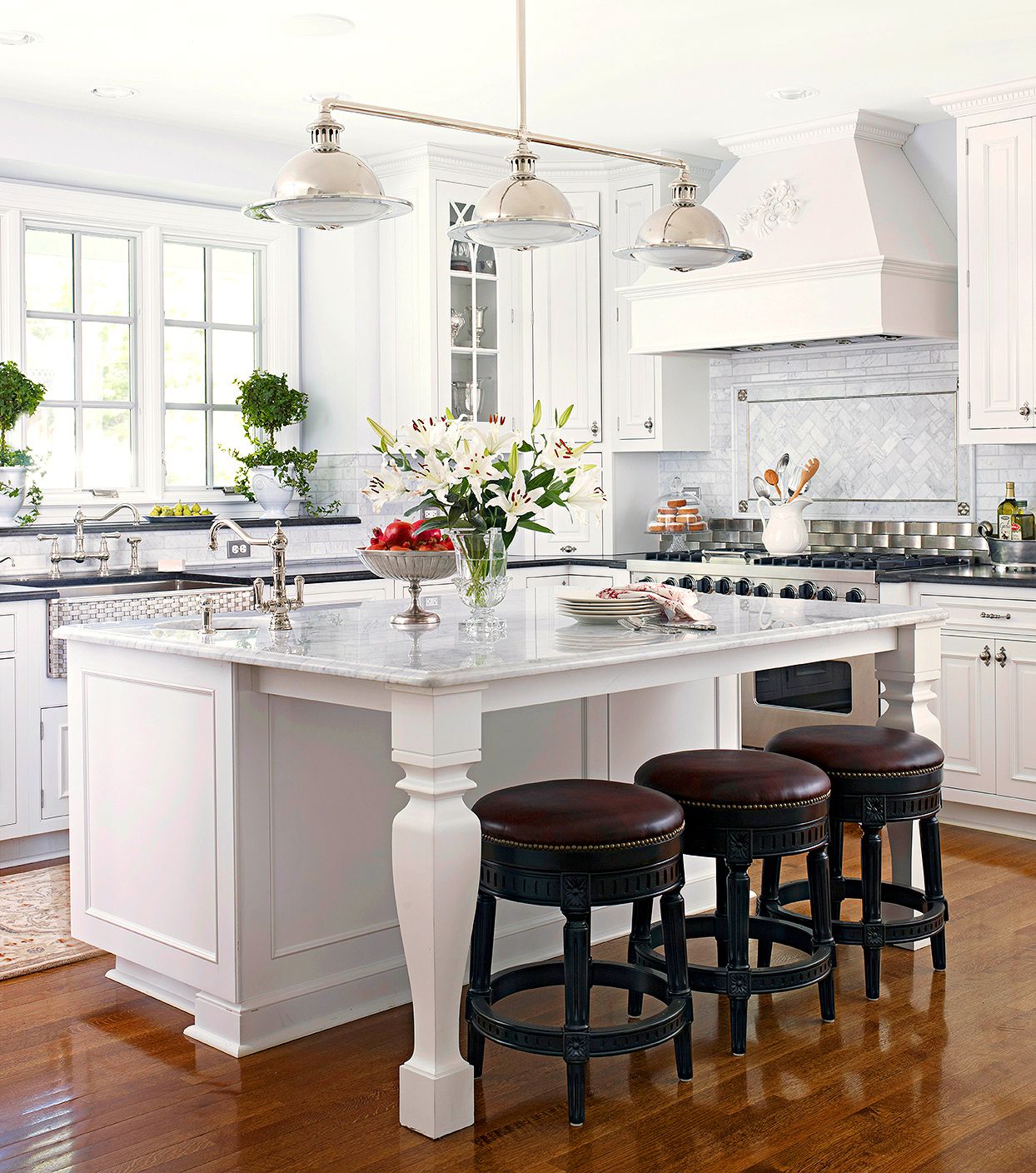 Classic white kitchen featuring a marble island with decorative legs, white cabinetry, chrome fixtures, and dark round stools.