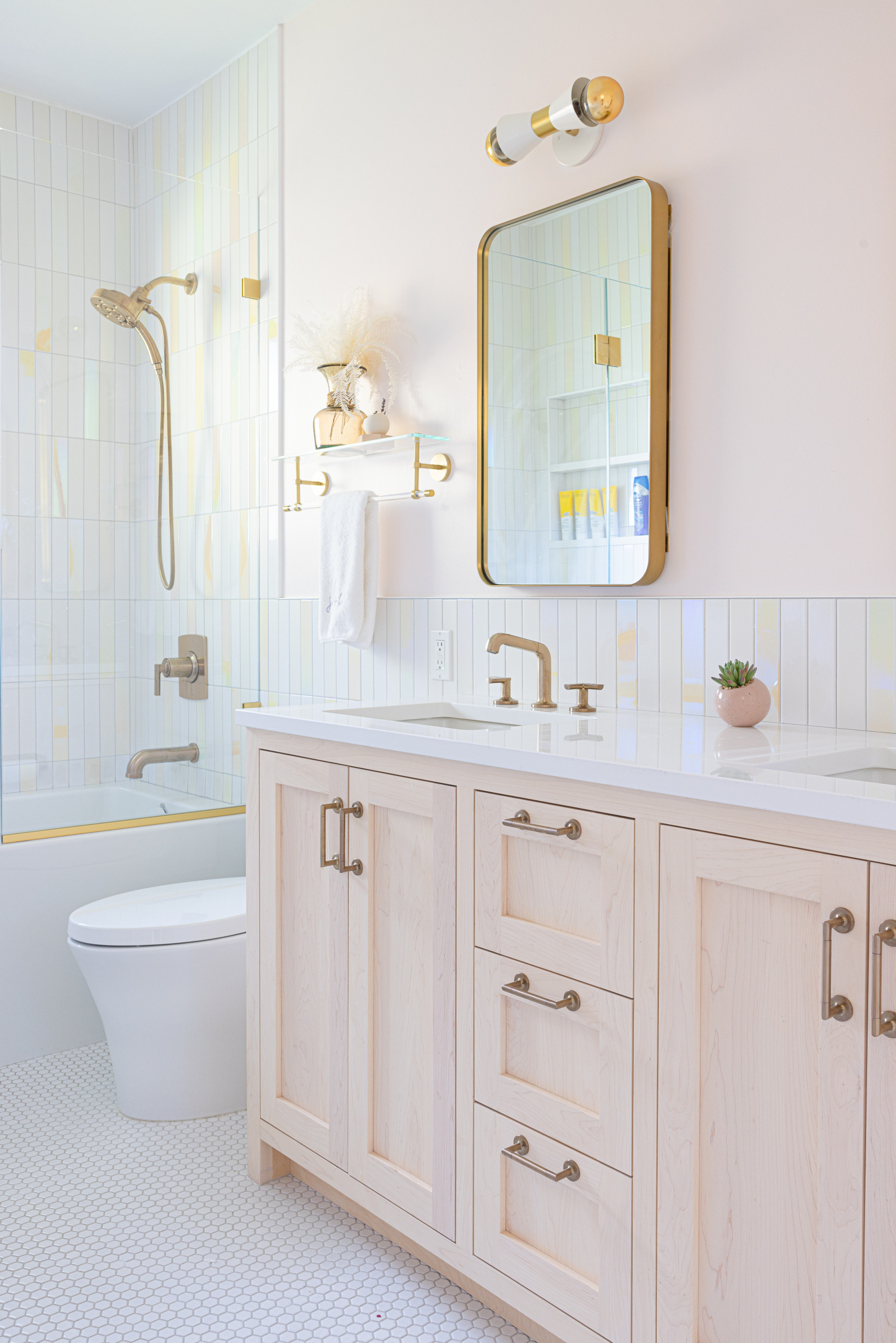 Bright modern bathroom with light wood vanity, white countertop, and brass fixtures.
