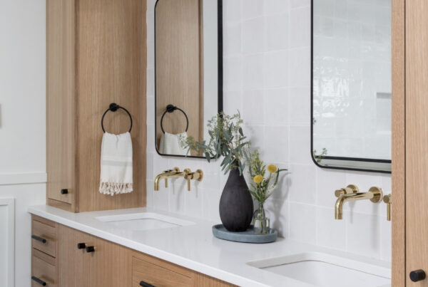 Modern bathroom with natural wood cabinetry, dual sinks, and wall-mounted brass faucets.