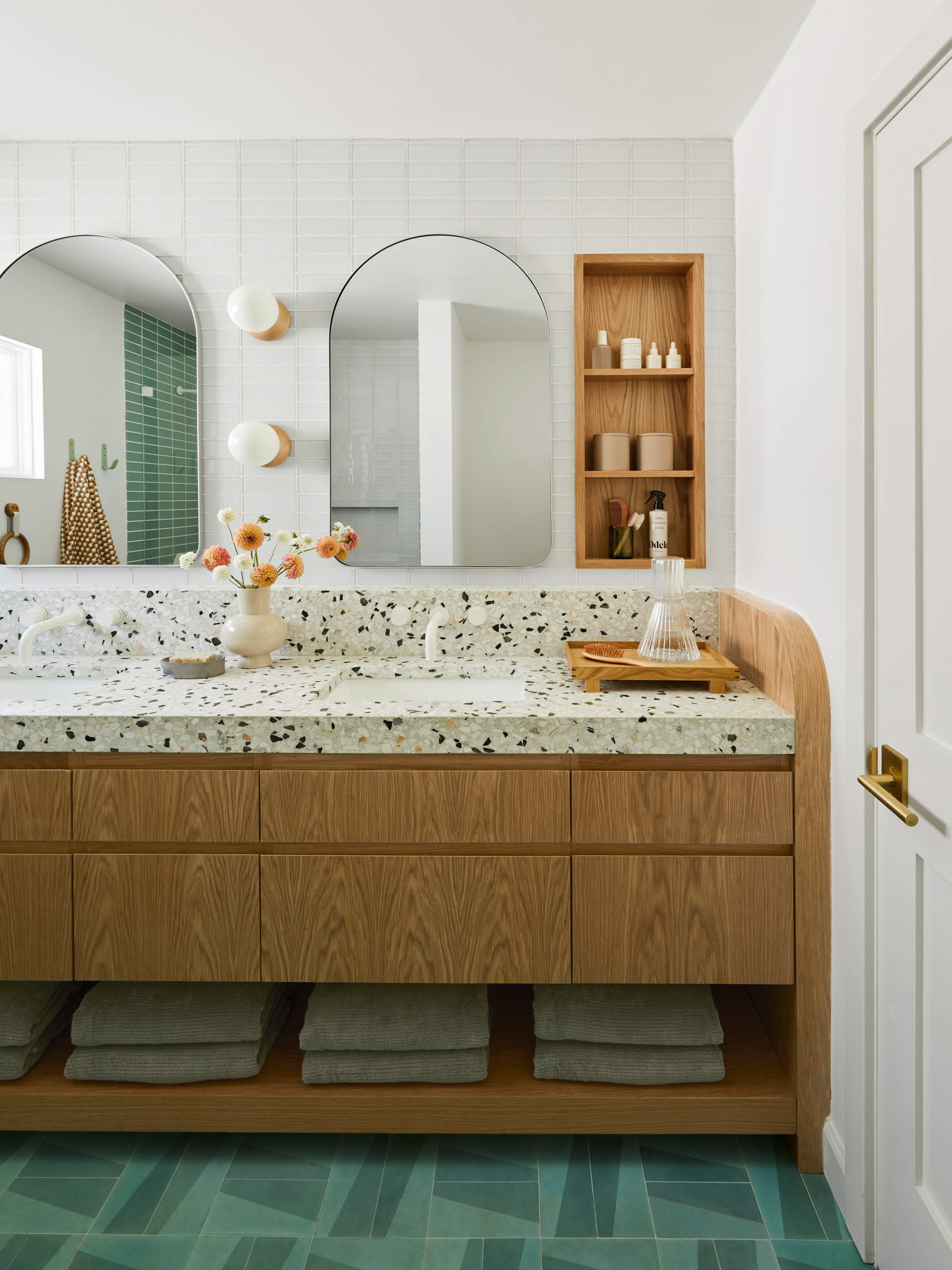 Modern bathroom vanity with terrazzo countertop, wood cabinetry, and arched mirrors.