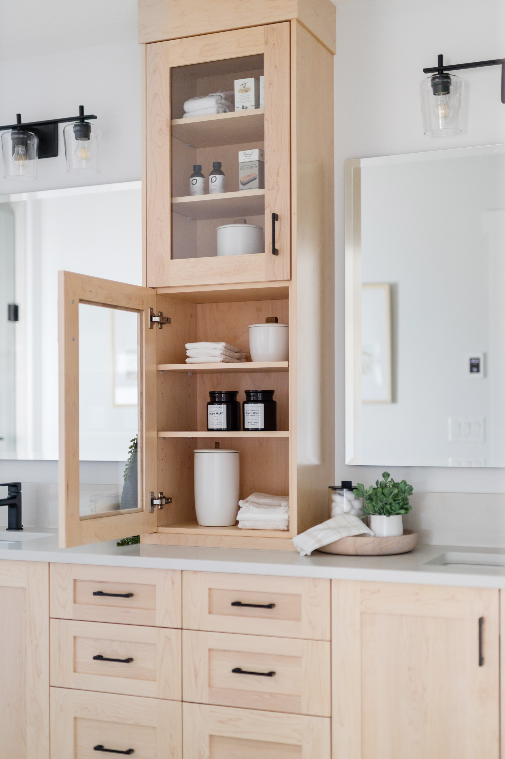 Light wood bathroom vanity with open cabinet showcasing towels, jars, and toiletries.