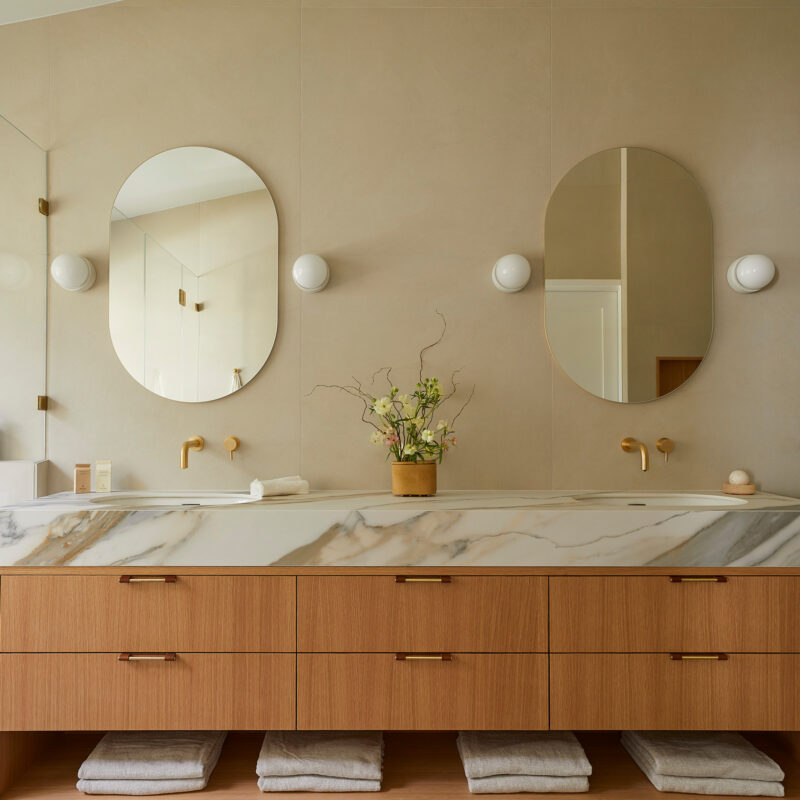 Elegant bathroom with marble countertop, wood vanity, and oval mirrors.