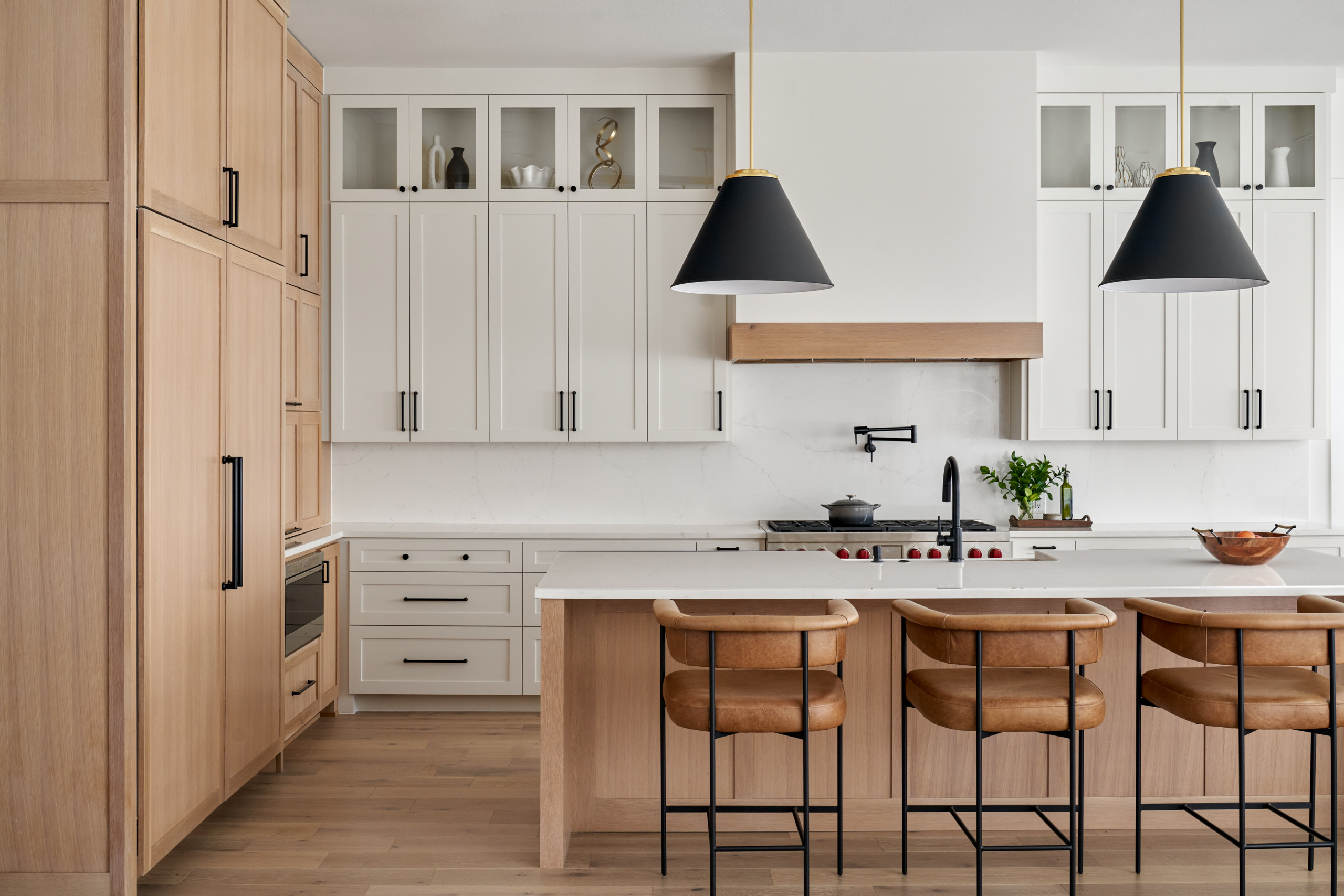 Modern kitchen with white shaker cabinets, light wood accents, and leather bar stools.