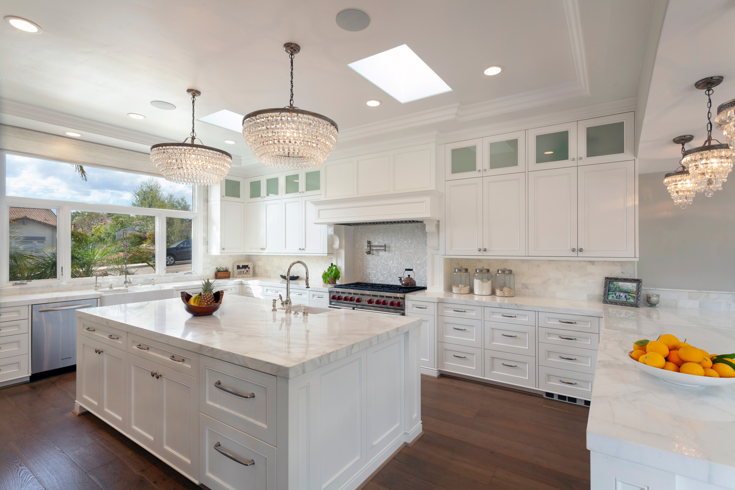 Elegant kitchen with white cabinetry, marble countertops, and crystal chandeliers.