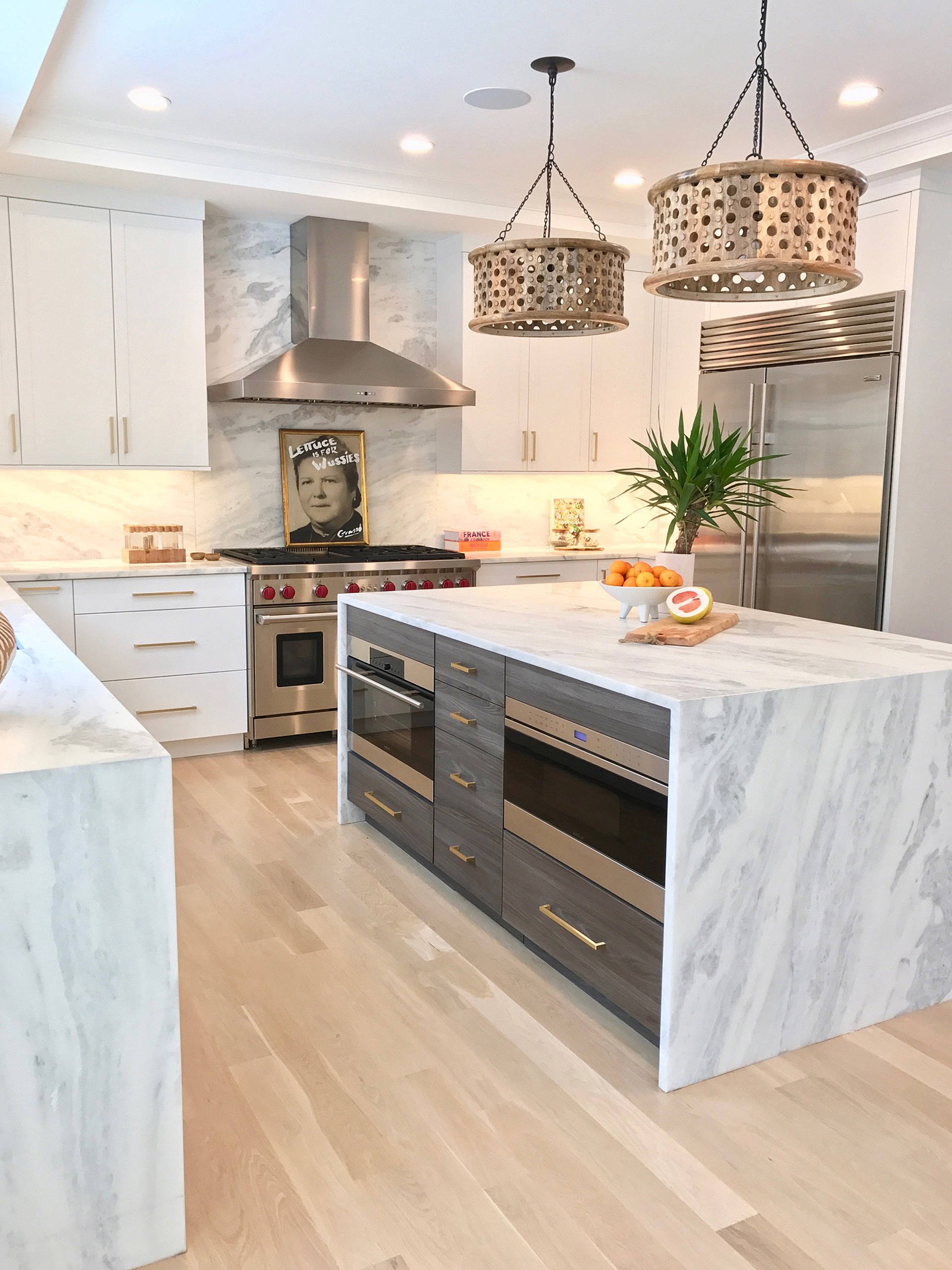 Modern kitchen with marble waterfall island, stainless steel appliances, and unique pendant lighting.
