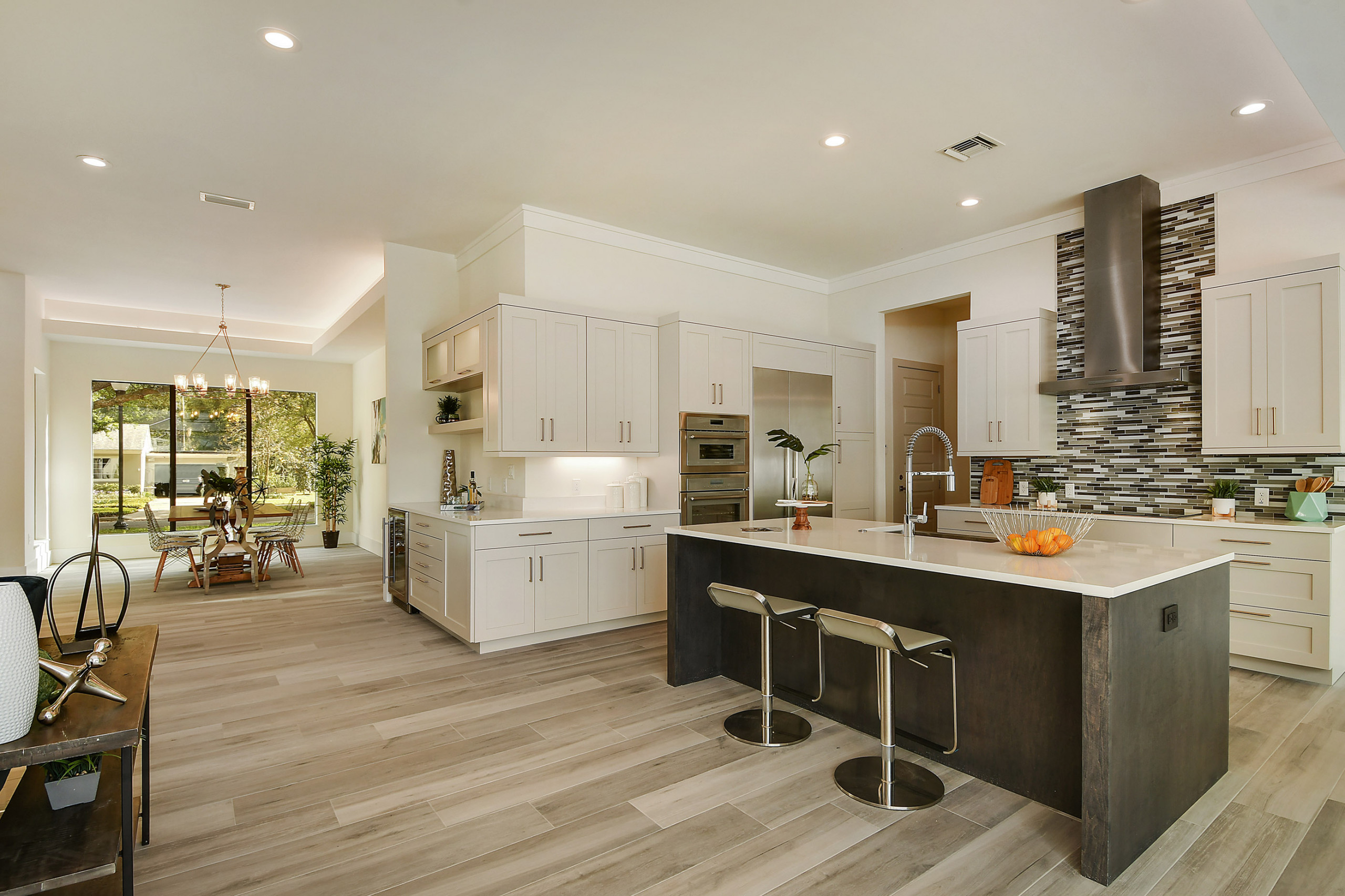 Modern open-concept kitchen with white cabinets, island, and mosaic backsplash.
