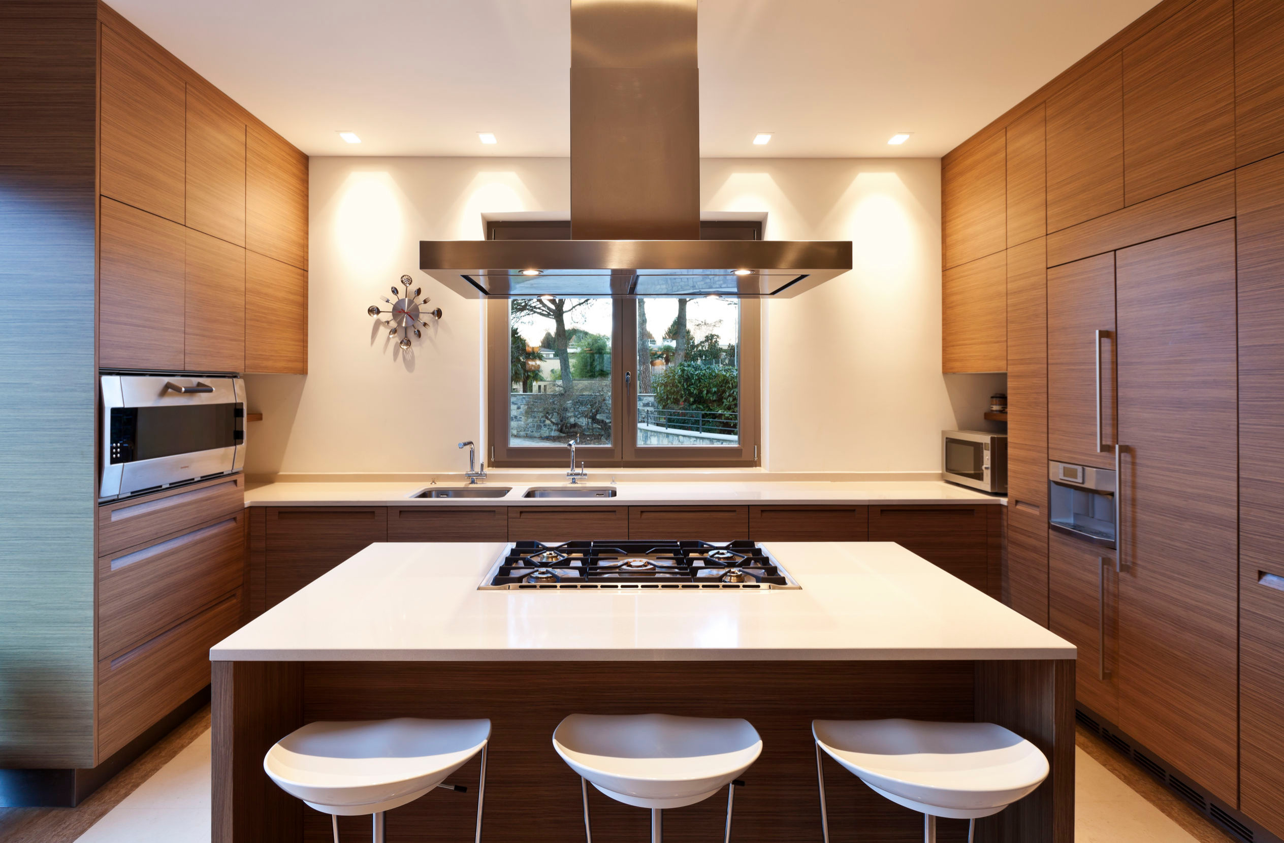 Modern kitchen with wood cabinets, island cooktop, and stainless steel appliances.