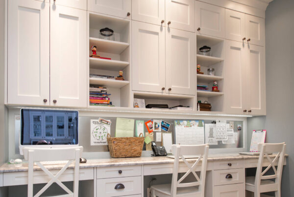 Built-in home office with white cabinets, three workstations, and overhead storage.