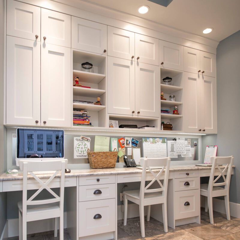 Built-in home office with white cabinets, three workstations, and overhead storage.