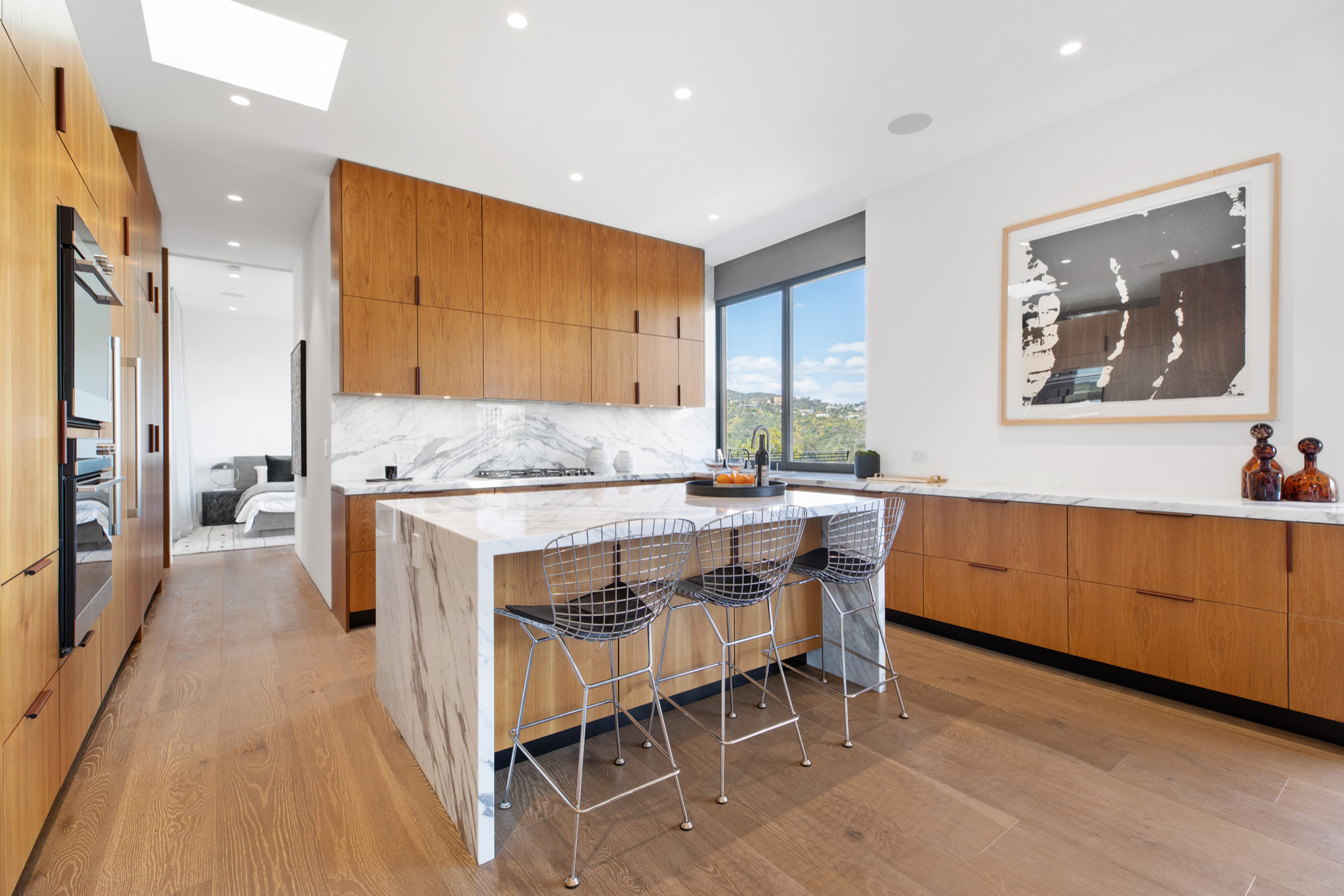 Modern kitchen with wood cabinetry, marble waterfall island, and metal bar stools.