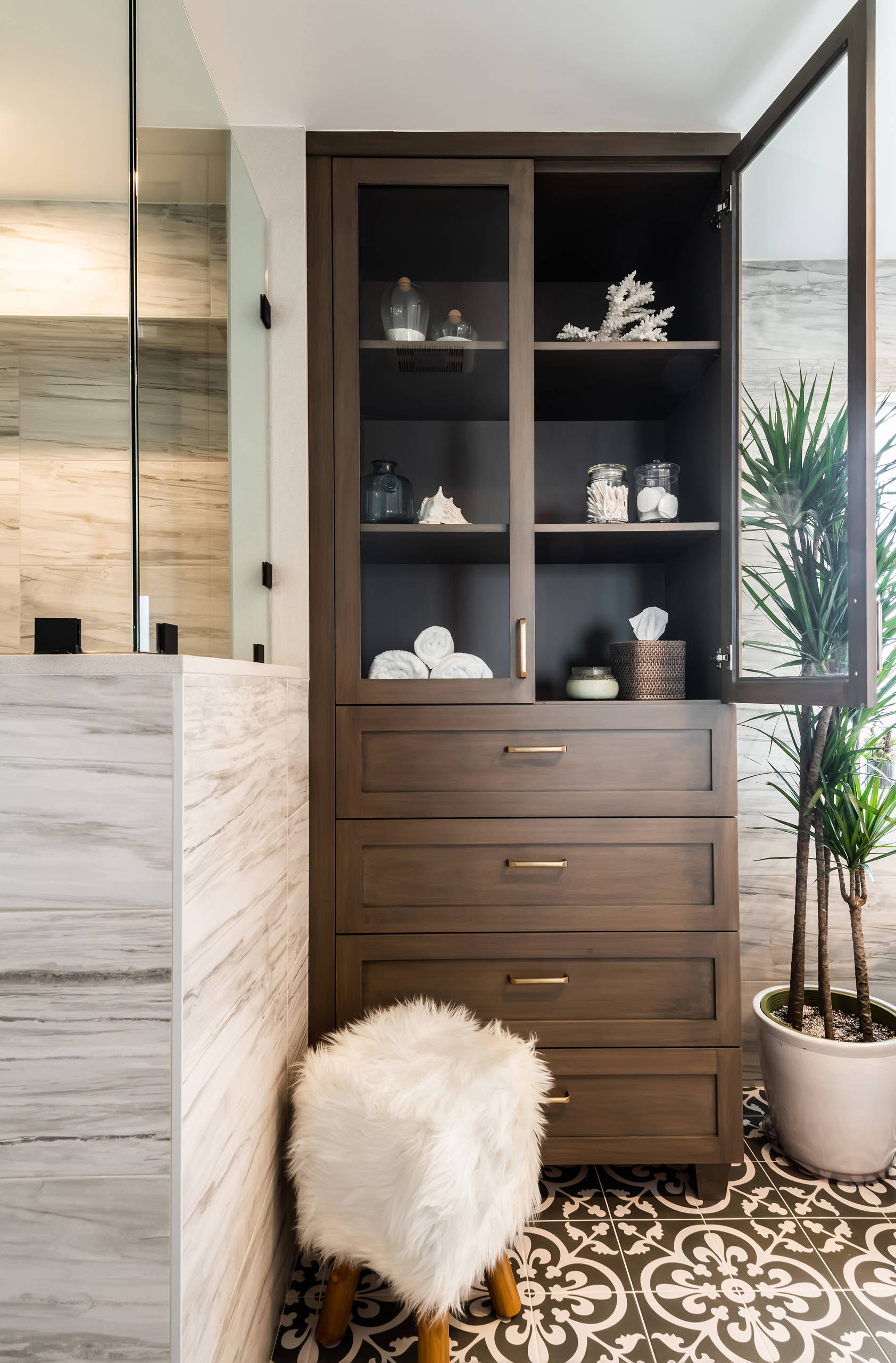 Modern bathroom storage cabinet with glass doors, wood drawers, and decorative accents.